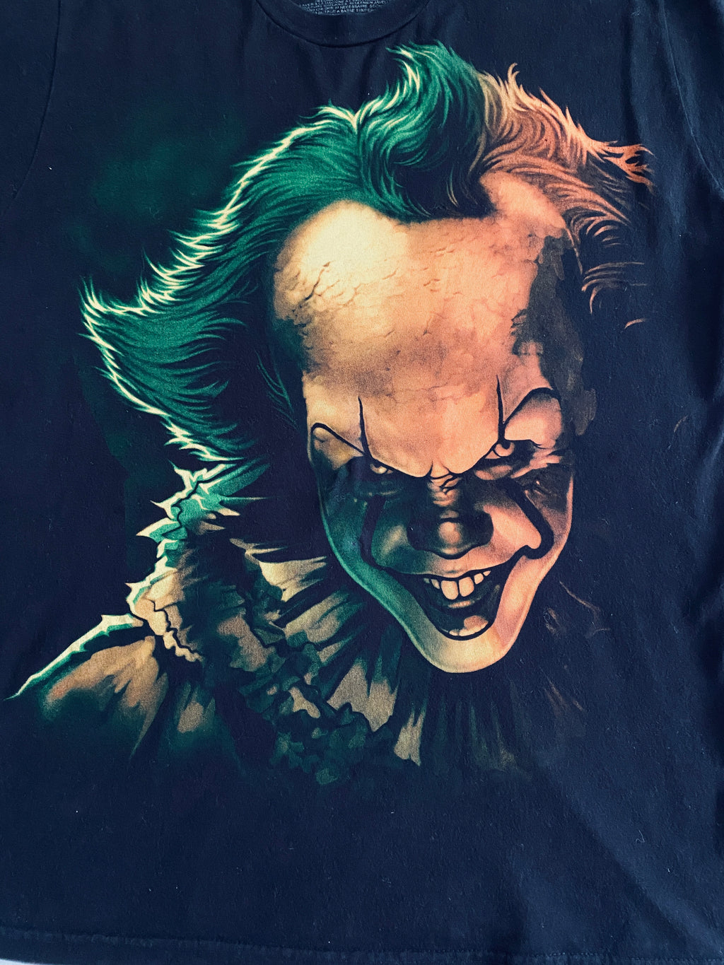 T-shirt IT Chapitre 2 – détail flocage face avant, portrait de Pennywise aux teintes joker vert émeraude et orange sur fond noir