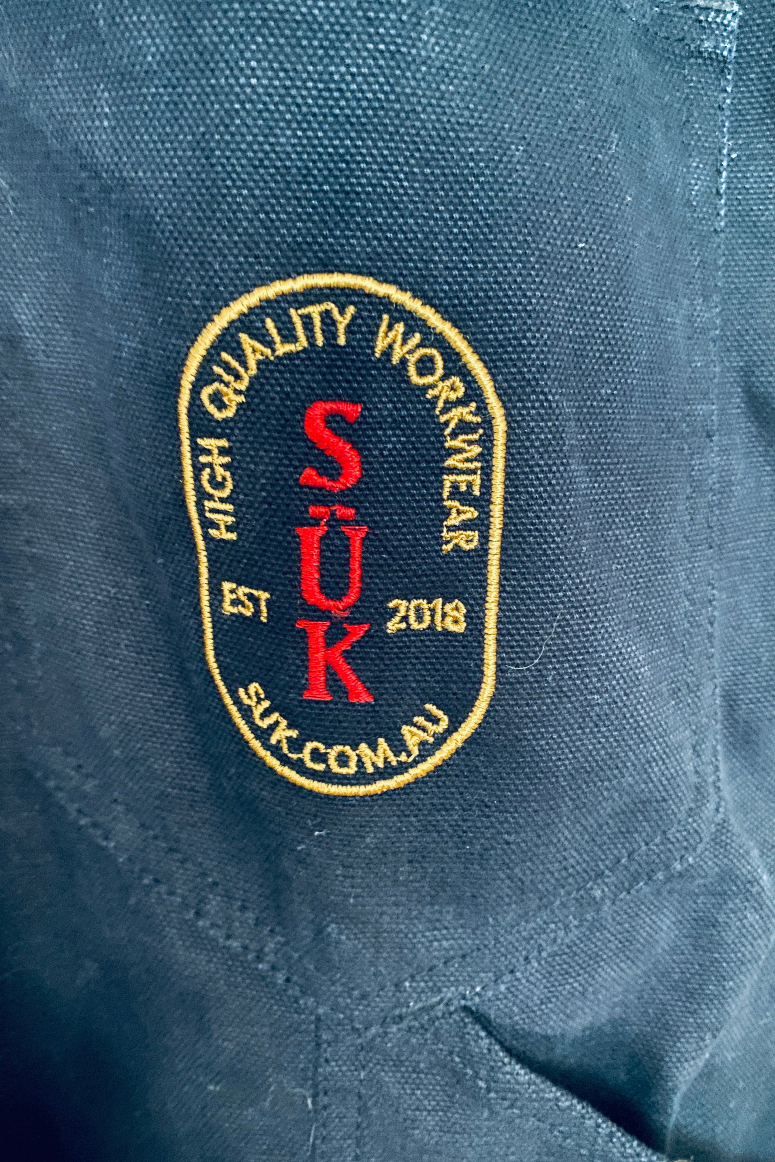 Vue de dos de la salopette SÜK, focus sur le patch brodé logo SÜK Workwear en rouge et or sur fond noir