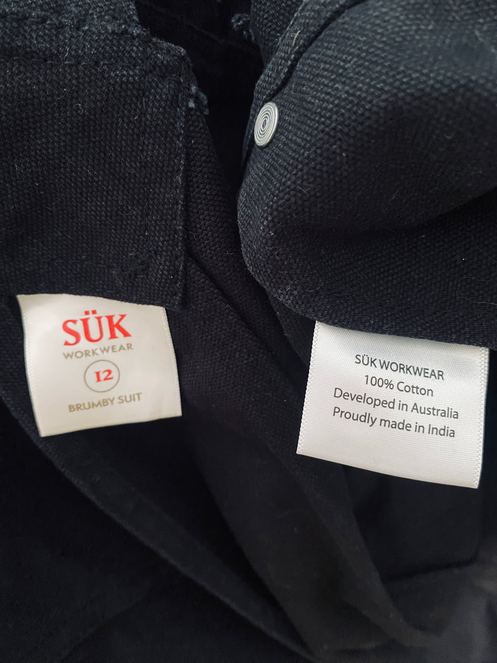 Détail des étiquettes intérieures de la salopette SÜK : marque, composition 100% coton et origine