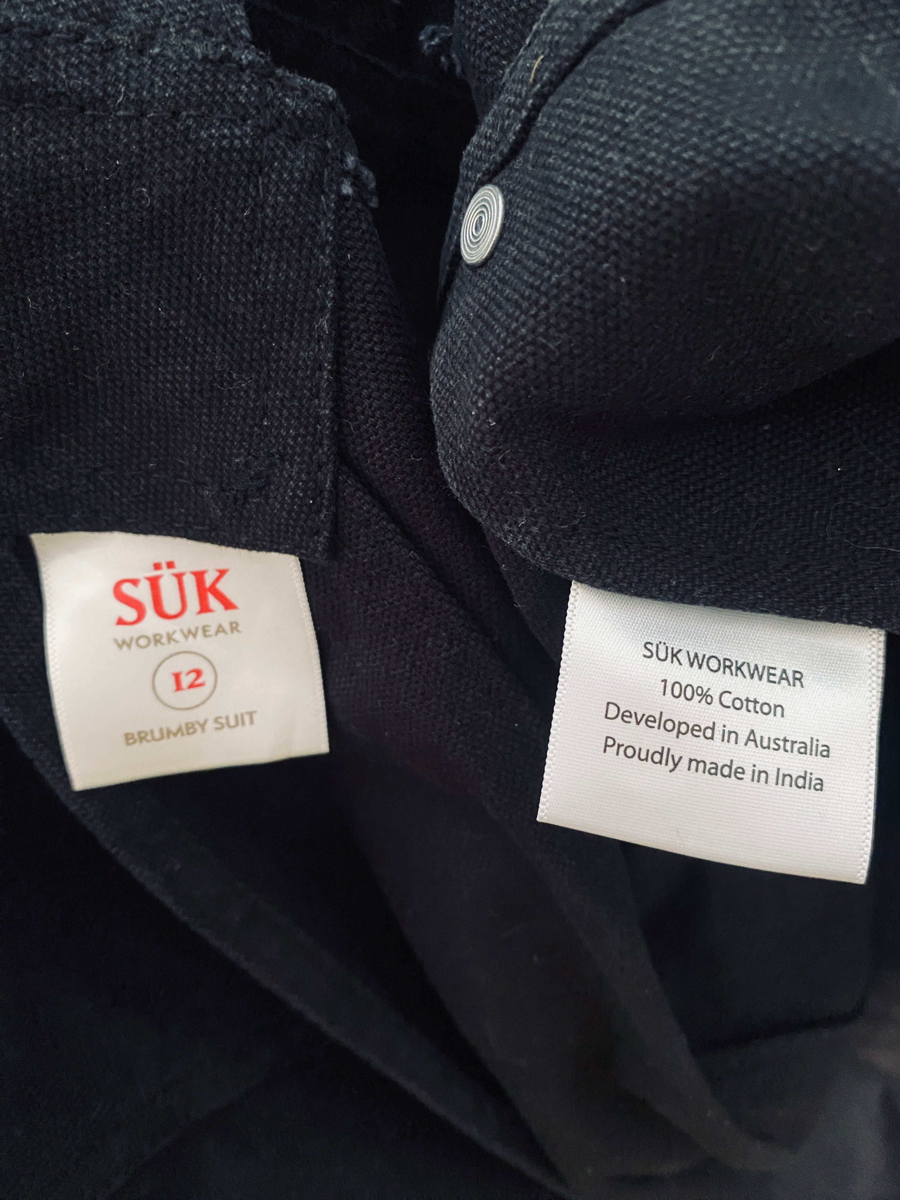 Détail des étiquettes intérieures de la salopette SÜK : marque, composition 100% coton et origine