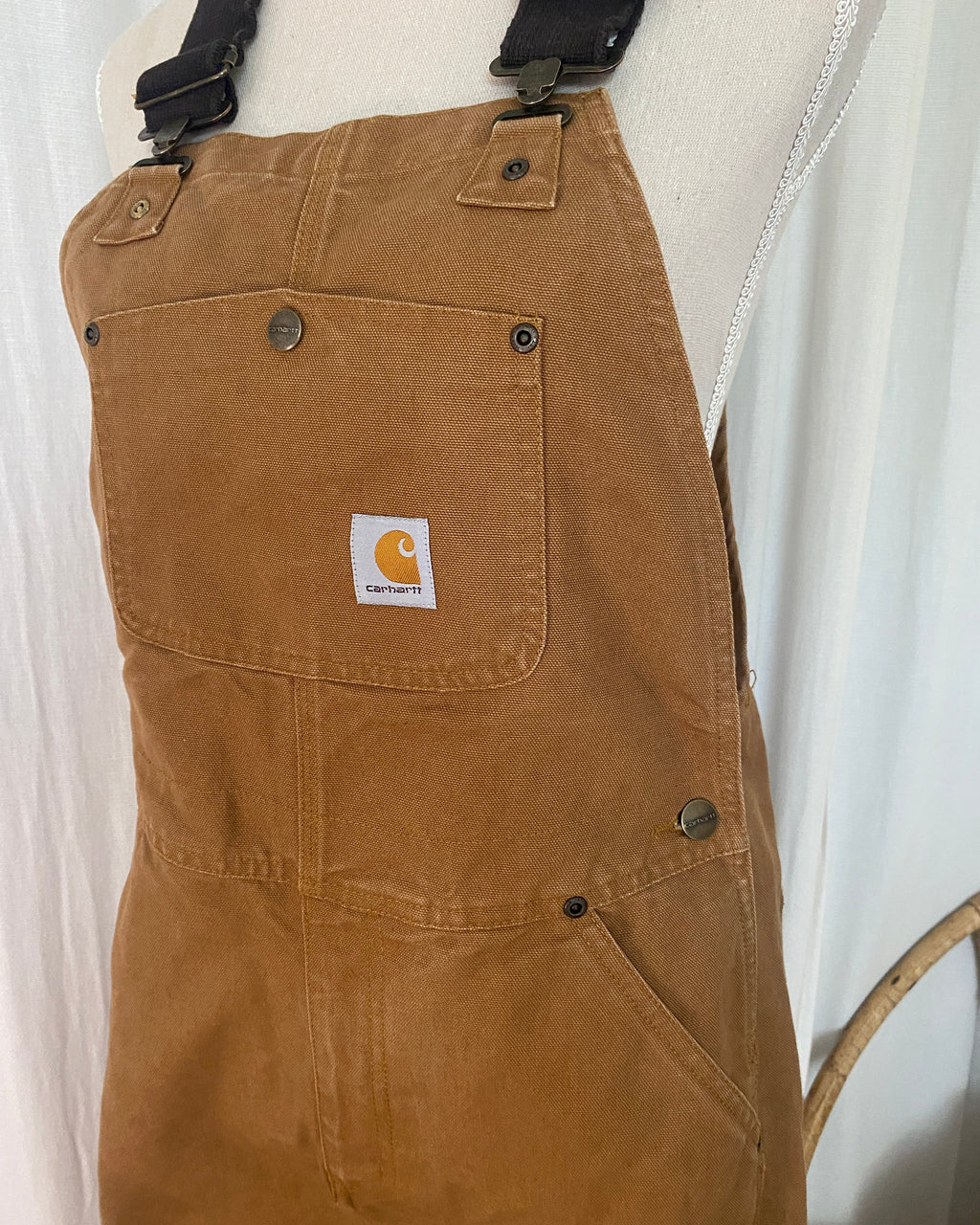 Vue de face de la salopette Carhartt, focus tablier avec poche plaquée, rivets bronze et patch logo woven