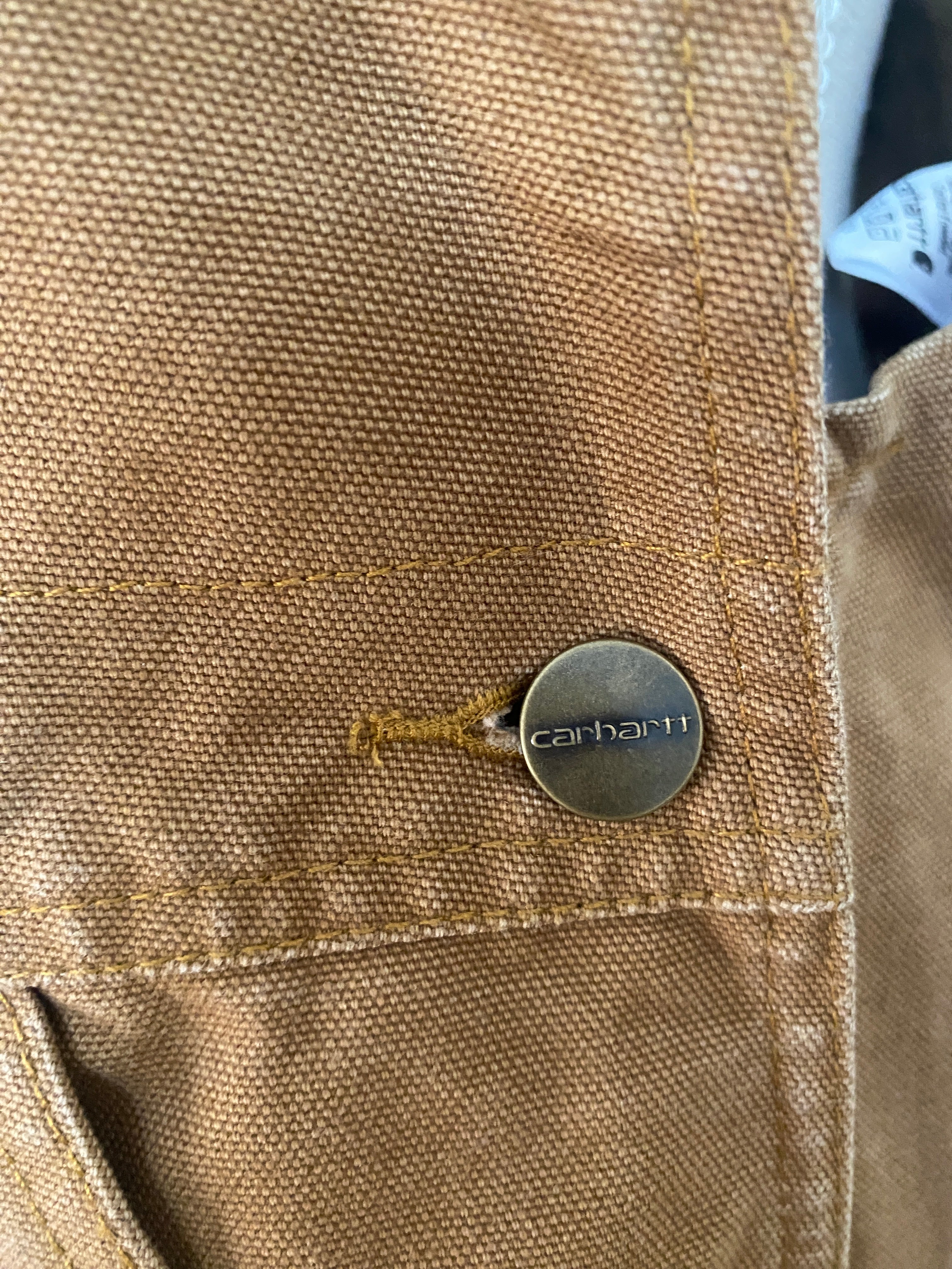 Détail bouton-pression gravé Carhartt en laiton bronze patiné sur denim Duck Brown